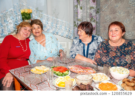 Four Russian friends, two in their 60s and two in their 70s, celebrate a special occasion together. They smile and pose for the camera at the dinner table, enjoying the moment with warmth and joy 120855629