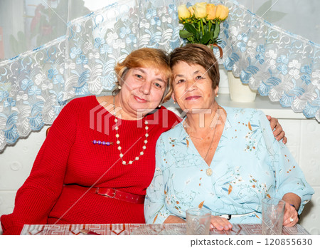 Two cheerful Russian women, aged 60 and 71, smile and embrace at home, celebrating their lifelong friendship. A warm moment of togetherness, perfect for themes of senior friendship and positive aging. Two cheerful Russian women, aged 60 and 71, smile and embrace at home, celebrating their lifelong friendship. A warm moment of togetherness, perfect for themes of senior friendship and positive aging. 120855630
