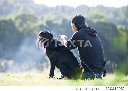 一位友好的男主人與他的大寵物狗依偎在戶外綠地裡,例如碼頭跑道 一位友好的男主人與他的大寵物狗依偎在戶外綠地裡,例如碼頭跑道 120856081