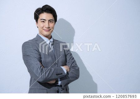 一位帥氣、清爽、年輕、真誠的商人，穿著西裝，雙臂交叉，看著鏡頭，淺藍色背景 120857693