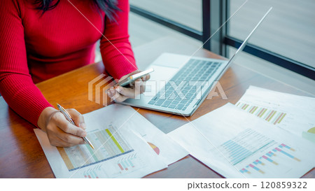 Woman holding a pen and smartphone while working at office, Close up shot hands of woman use pen to analyze graphs and business data, Women working on laptop to analysis finance of project. 120859322