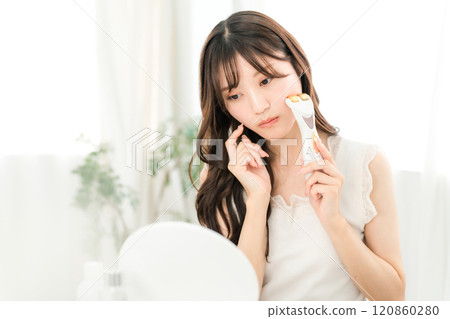 一位年輕的亞洲女性在用臉部按摩器按摩時擔心自己的皮膚(皮膚護理) 一位年輕的亞洲女性在用臉部按摩器按摩時擔心自己的皮膚(皮膚護理) 120860280