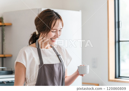 Young Asian woman wearing an apron drinking coffee in the kitchen/dining room 120860809