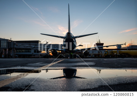 Ground handling of a passenger airplane parked to a jet bridge with reflection in a puddle Ground handling of a passenger airplane parked to a jet bridge with reflection in a puddle 120860815