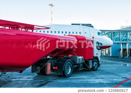 The red tanker refueling the aircraft parked to a boarding bridge at the airport apron The red tanker refueling the aircraft parked to a boarding bridge at the airport apron 120860827