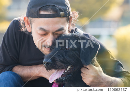 Close-up of a friendly male owner cuddling with his large pet dog in a setting of autumn leaves or foliage Close-up of a friendly male owner cuddling with his large pet dog in a setting of autumn leaves or foliage 120862587