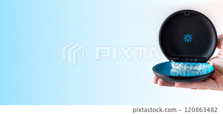 Banner, hand holding Invisalign transparent braces on blue background with copy space. Orthodontic invisible retainers and aligners 120863482