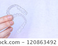 Hand holding Invisalign transparent braces on white background with copy space. Invisible retainers and aligners 120863492