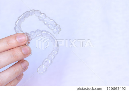Hand holding Invisalign transparent braces on white background with copy space. Invisible retainers and aligners Hand holding Invisalign transparent braces on white background with copy space. Invisible retainers and aligners 120863492