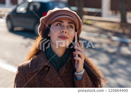Portrait of a young Caucasian woman in a coat and beret, with braces on her teeth, talking on the street on a smartphone. Urban lifestyle Portrait of a young Caucasian woman in a coat and beret, with braces on her teeth, talking on the street on a smartphone. Urban lifestyle 120864400