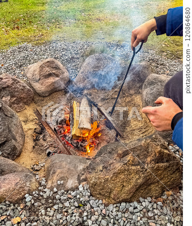 Campfire in Outdoor Retreat, Hands Stoking Flames Surrounded by Rocks and Gravel. High quality photo 120864680