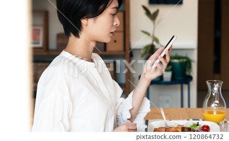 一個女人一邊吃飯一邊看一部智能手機 120864732