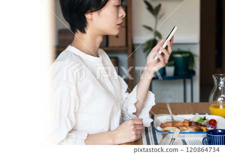 一個女人一邊吃飯一邊看一部智能手機 120864734