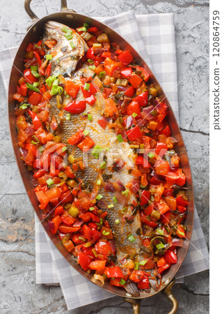 Whole sea bass stewed with bell pepper, onion, tomatoes, garlic and celery close-up in a frying pan. Vertical top view 120864759