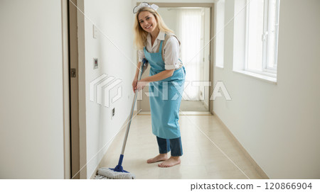 Smiling cleaning lady in uniform mopping wooden floor in bright hallway, professional home cleaner with blue gloves, housemaid working indoors, domestic cleaning service staff Smiling cleaning lady in uniform mopping wooden floor in bright hallway, professional home cleaner with blue gloves, housemaid working indoors, domestic cleaning service staff 120866904