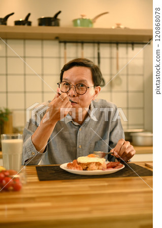 Happy middle aged man enjoys a homemade breakfast at wooden kitchen counter 120868078