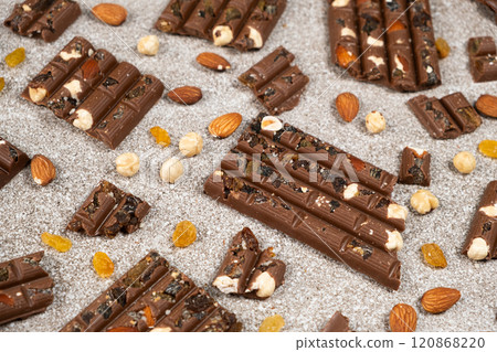 Broken chocolate pieces with nuts and raisins on a stone background Broken chocolate pieces with nuts and raisins on a stone background 120868220