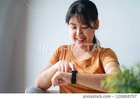 Happy young woman is using smartwatch on her wrist to check health data, notifications, set alarm. Happy young woman is using smartwatch on her wrist to check health data, notifications, set alarm. 120868707