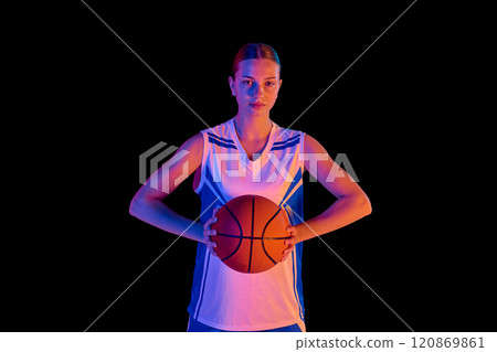 Portrait of focused teen girl, basketball player standing and posing with ball in hands against black studio background in neon light Portrait of focused teen girl, basketball player standing and posing with ball in hands against black studio background in neon light 120869861