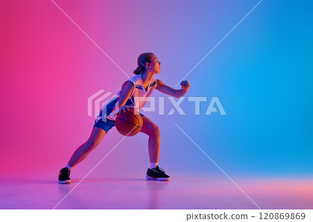 Dynamic image of young teen girl, basketball player in motion with ball, training, playing against gradient pink blue background in neon light 120869869