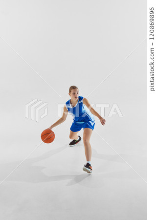 Focused teen girl, basketball player in blue uniform in motion with ball, training against white studio background. Dribbling. Focused teen girl, basketball player in blue uniform in motion with ball, training against white studio background. Dribbling. 120869896