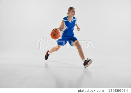 Young teen girl in blue uniform, in motion with ball, playing basketball, training against white studio background Young teen girl in blue uniform, in motion with ball, playing basketball, training against white studio background 120869914