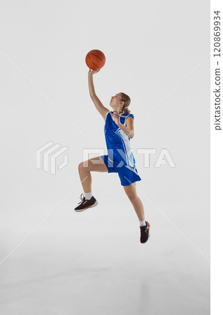 Slam dunk. Full-length vertical image of young teen girl in blue uniform, basketball player in motion, playing, training against white studio background Slam dunk. Full-length vertical image of young teen girl in blue uniform, basketball player in motion, playing, training against white studio background 120869934