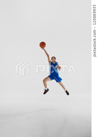 Slam dunk. Full-length vertical image of young teen girl in blue uniform, basketball player in motion, playing, training against white studio background Slam dunk. Full-length vertical image of young teen girl in blue uniform, basketball player in motion, playing, training against white studio background 120869935