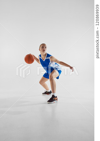 Young motivated and focused teen girl, basketball player in blue uniform, with ball, training against white studio background Young motivated and focused teen girl, basketball player in blue uniform, with ball, training against white studio background 120869939