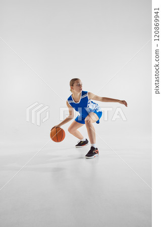 Dynamic image of teen girl in motion with ball, wearing blue uniform, competing for the victory, playing against white studio background Dynamic image of teen girl in motion with ball, wearing blue uniform, competing for the victory, playing against white studio background 120869941