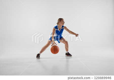 Competitive young girl, basketball player in blue uniform in motion with ball, training with motivation to win against white studio background Competitive young girl, basketball player in blue uniform in motion with ball, training with motivation to win against white studio background 120869946