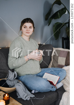 Pregnant woman enjoying a warm drink in cozy home setting. Comfort, relaxation, and calm during pregnancy. 120871162