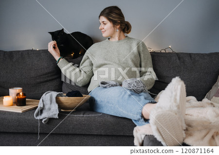 Pregnant woman knitting with black cat beside, preparing handmade baby items. Cozy nesting, relaxation, and mindful pregnancy. Pregnant woman knitting with black cat beside, preparing handmade baby items. Cozy nesting, relaxation, and mindful pregnancy. 120871164