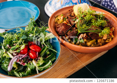 Traditional Moroccan tagine with lamb, vegetables, and nuts served with a fresh side salad. Highlights vibrant Mediterranean flavors and culinary artistry. 120871186