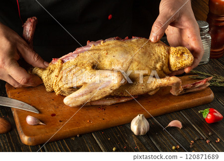 A chef skillfully prepares a whole duck, showcasing culinary artistry in a warm kitchen. Fresh ingredients surround the wooden cutting board, ready for a delicious meal A chef skillfully prepares a whole duck, showcasing culinary artistry in a warm kitchen. Fresh ingredients surround the wooden cutting board, ready for a delicious meal 120871689
