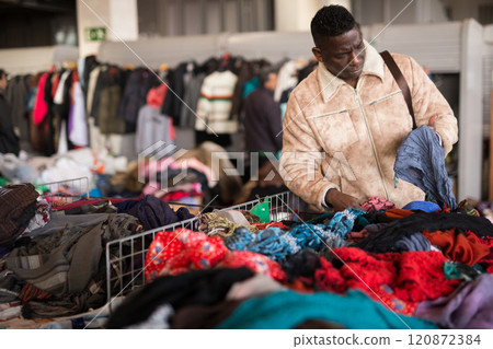 Man looks at second-hand clothes at a flea market Man looks at second-hand clothes at a flea market 120872384