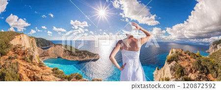 Beautiful woman in white dress stands on a cliff with the view to the famous shipwreck beach, Navagio, on Zakynthos island, Greece Beautiful woman in white dress stands on a cliff with the view to the famous shipwreck beach, Navagio, on Zakynthos island, Greece 120872592