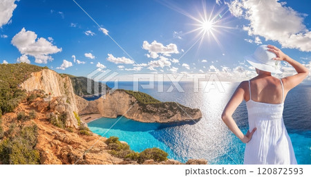 Beautiful woman in white dress stands on a cliff with the view to the famous shipwreck beach, Navagio, on Zakynthos island, Greece Beautiful woman in white dress stands on a cliff with the view to the famous shipwreck beach, Navagio, on Zakynthos island, Greece 120872593