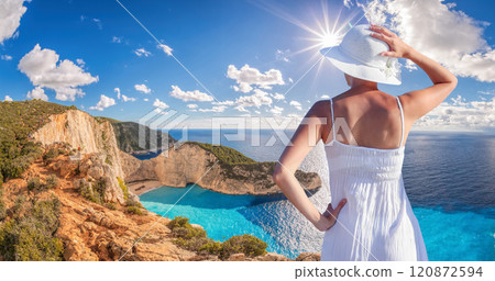 Beautiful woman in white dress stands on a cliff with the view to the famous shipwreck beach, Navagio, on Zakynthos island, Greece 120872594