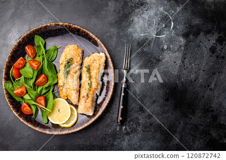Roast Cod fish fiilets, white fish meat on plate with salad. Black background. top view 120872742
