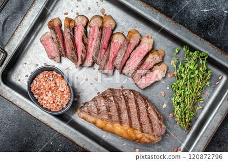 Grilled and sliced brazilian Picanha steak, cup rump beef meat steak on a steel serving tray with herbs. Black background. Top view. Copy space 120872796