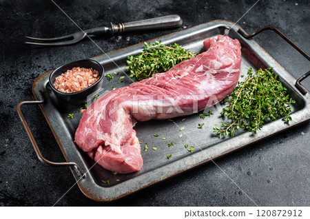 Raw pork tenderloin fillet meat in steel tray with herbs. Black background. Top view 120872912