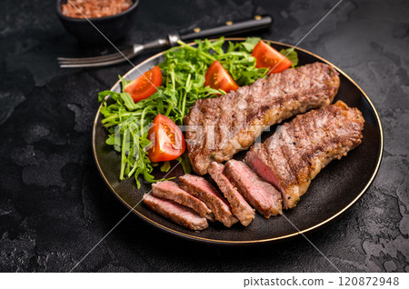 Grilled Steak from Black Angus beef meat on a plate with salad. black background. top view Grilled Steak from Black Angus beef meat on a plate with salad. black background. top view 120872948