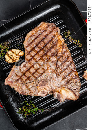 Grilled T-bone, t bone beef meat Steak on a grill skillet. Black background. Top view 120872954