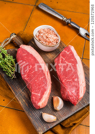 Cap Rump steak, raw beef meat steak with thyme and salt on wooden butcher board. Orange background. Top view 120872968