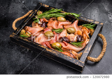 Prosciutto ham or Jamon Serrano with rosemary and olives in wooden tray. black background. top view Prosciutto ham or Jamon Serrano with rosemary and olives in wooden tray. black background. top view 120872980