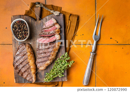 BBQ Roast brazilian Picanha steak, cup rump beef meat steak on a wooden serving board. Orange background. Top view BBQ Roast brazilian Picanha steak, cup rump beef meat steak on a wooden serving board. Orange background. Top view 120872990
