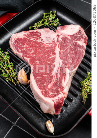 Raw T-bone or porterhouse beef meat Steak with thyme in a grill skillet ready for cooking. Black background. Top view 120873068