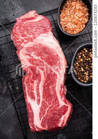 Ready for cooking Chuck eye roll steak, fresh raw beef meat on a rack. black background. top view 120873283