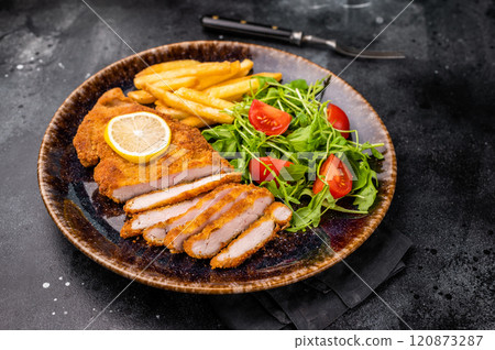 Roast viennese schnitzel steak, breaded meat with salad and french fry on a plate. black background. top view Roast viennese schnitzel steak, breaded meat with salad and french fry on a plate. black background. top view 120873287